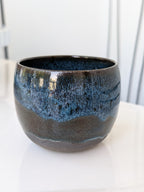 Ceramic pot with blue and black glaze on a white surface