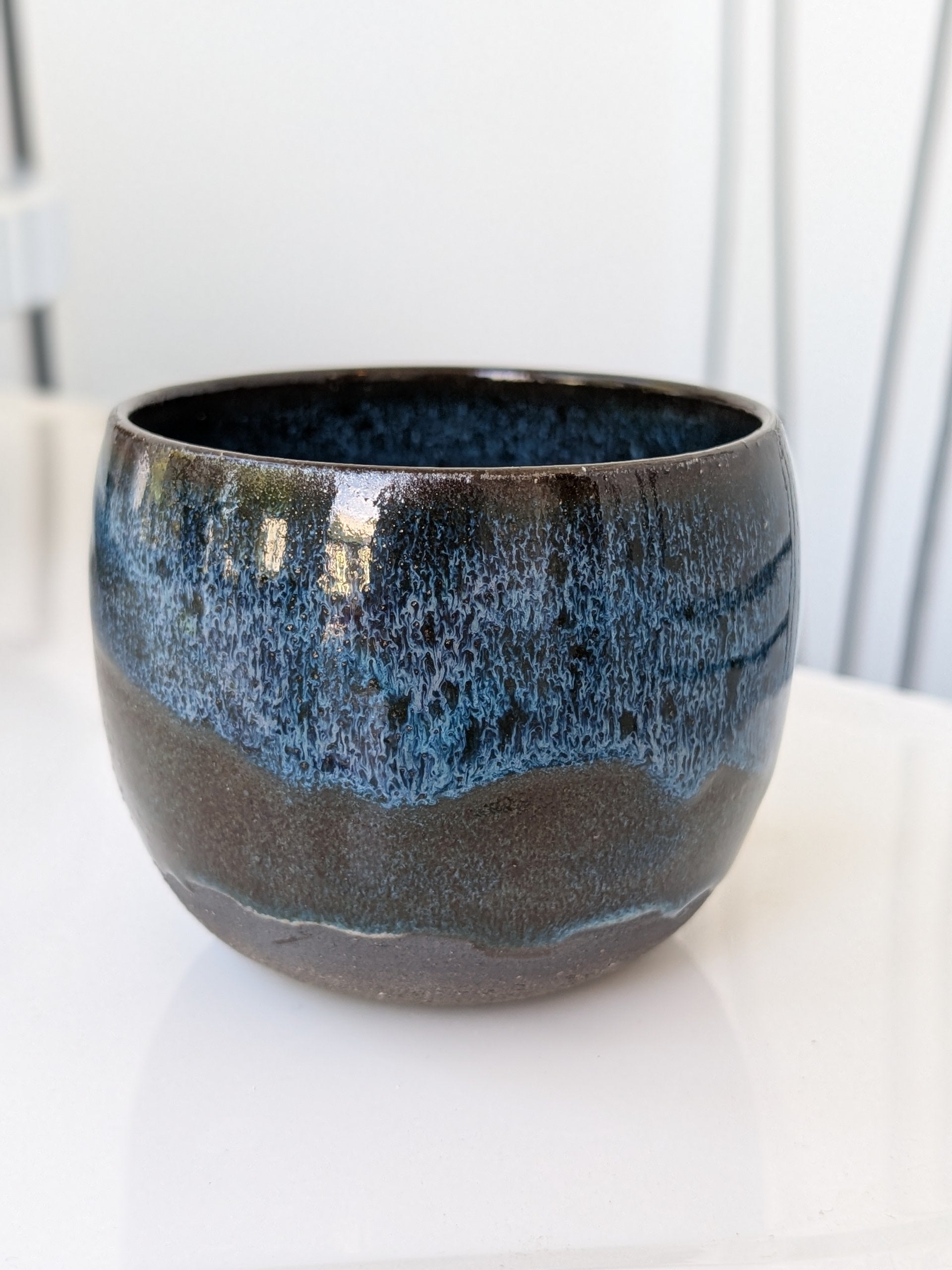 Ceramic pot with blue and black glaze on a white surface
