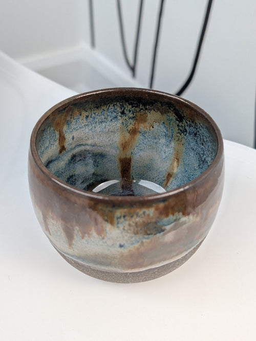 Handmade brown, white, and blue glazed ceramic cup, isometric view