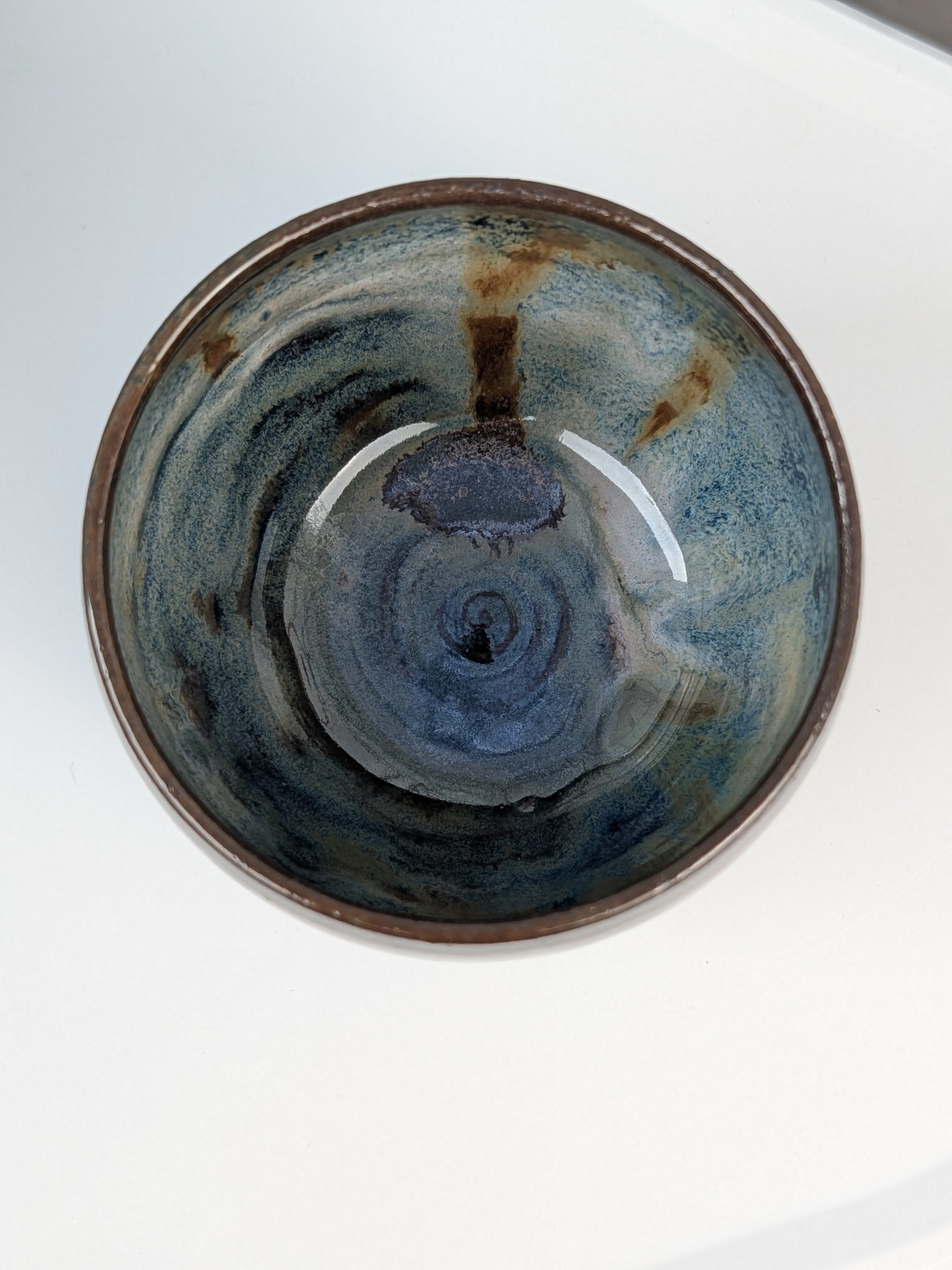 Handemade brown, white, and blue glazed ceramic cup, top view with swirl pattern inside