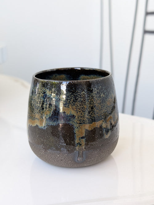 Black ceramic cup with speckled pattern on a white surface