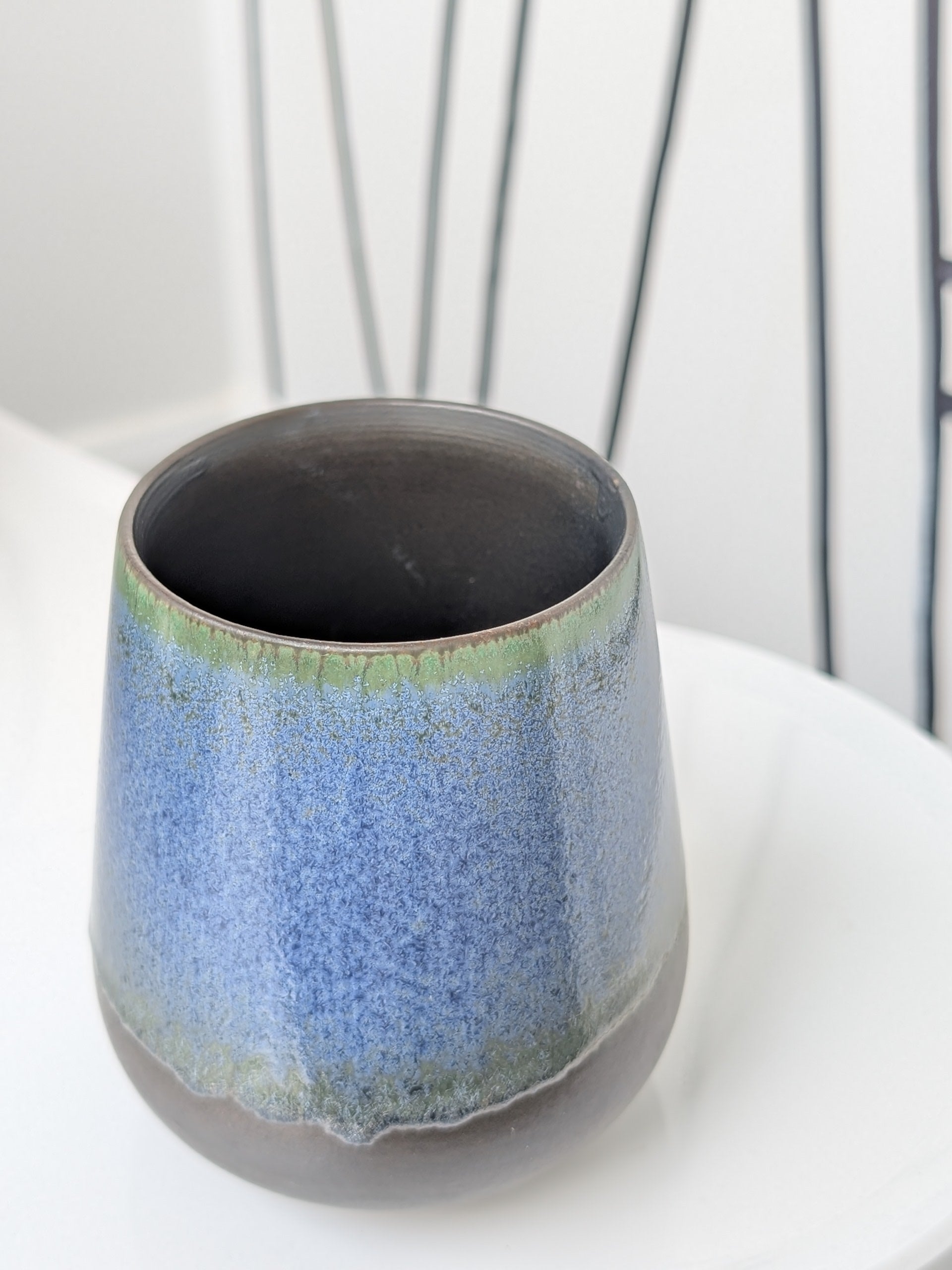 Ceramic cup with blue and green glaze on a white surface