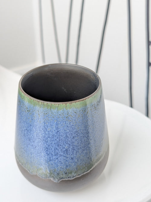 Ceramic cup with blue and green glaze on a white surface