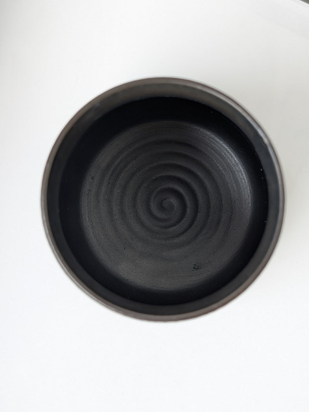 Black ceramic dish with spiral pattern on a white background