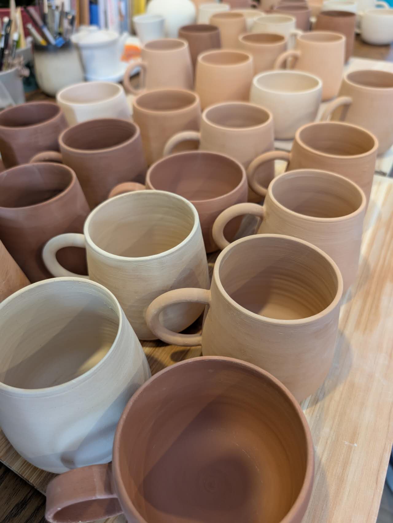 Collection of ceramic mugs in various colors on a wooden surface