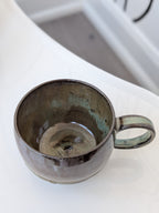 Handmade brown and green glazed ceramic cup, isometric view