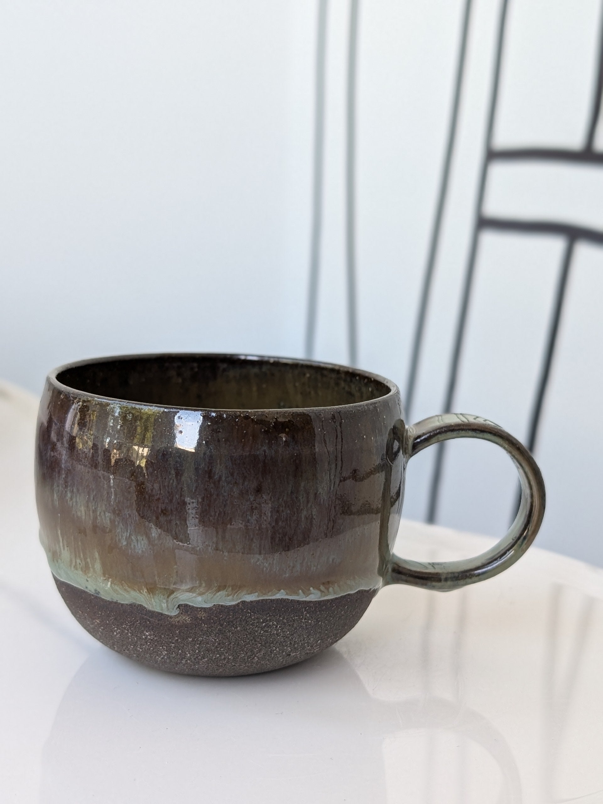 Handmade brown and green glazed ceramic cup, side view with handle
