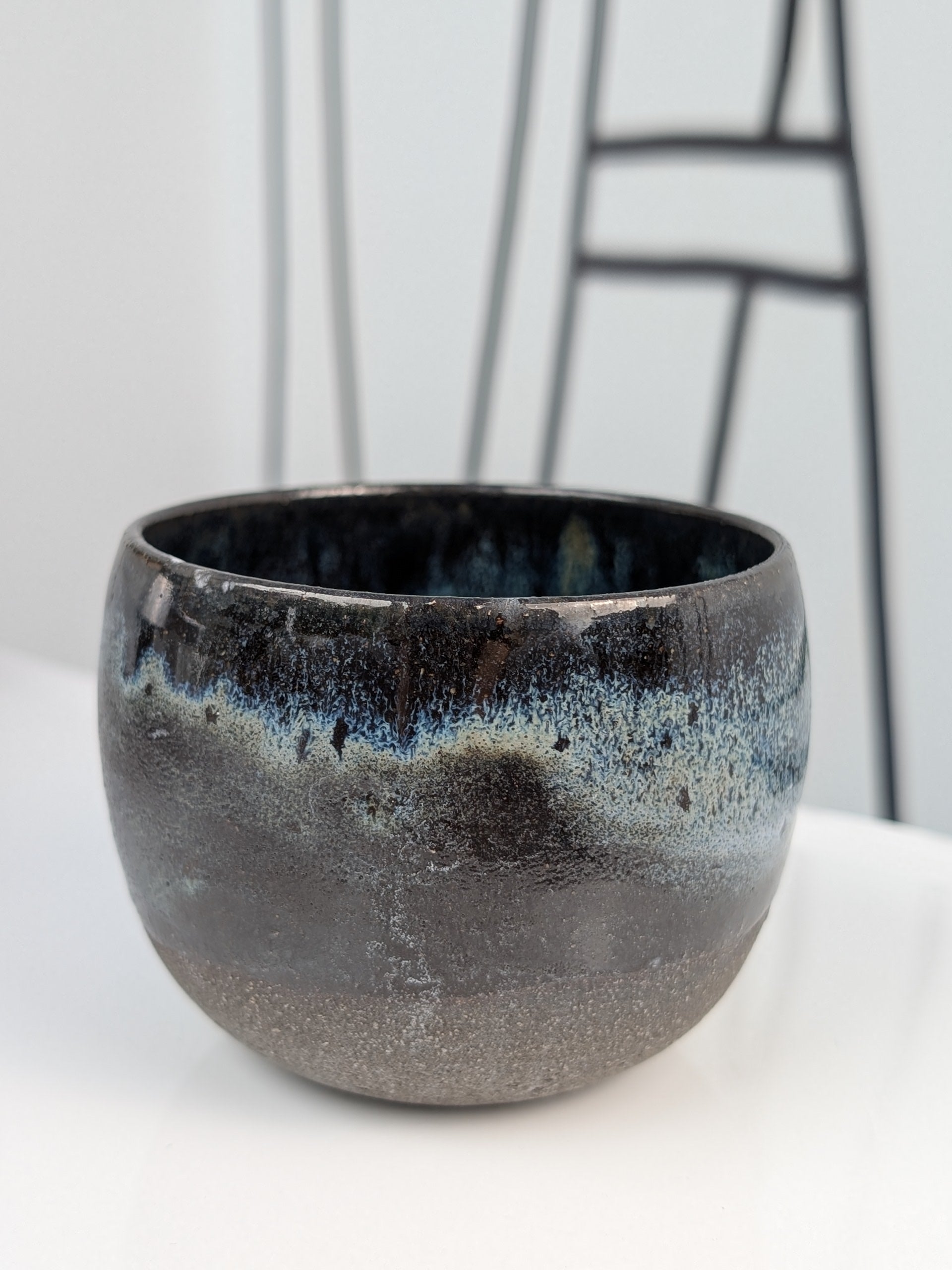 Handmade black, white, and blue glazed ceramic cup, front view