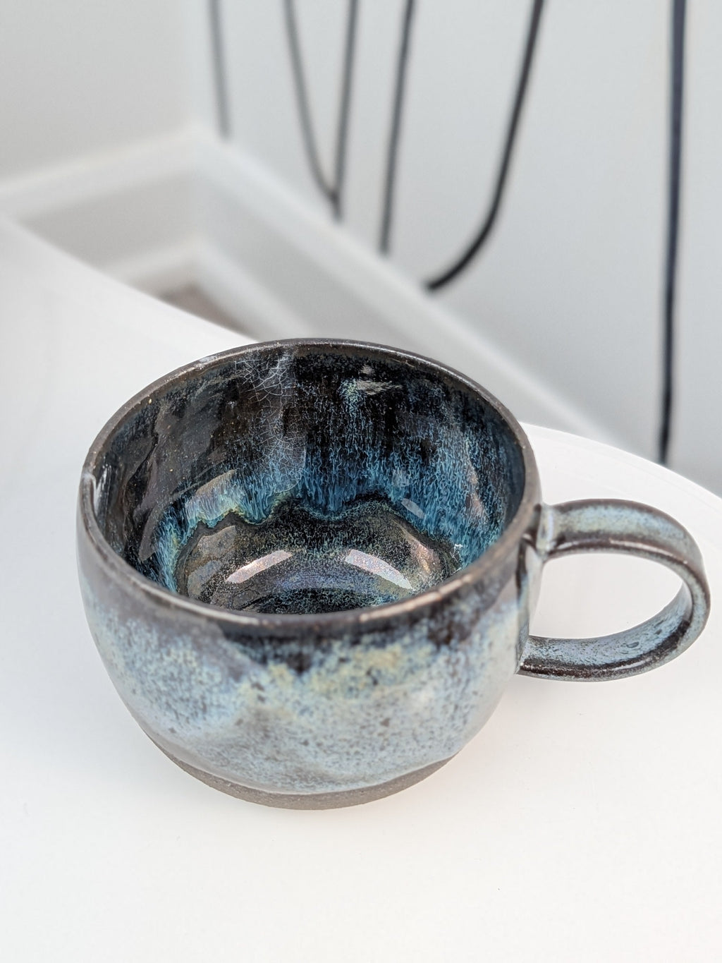 Handmade black, white, and blue glazed ceramic cup, isometric view