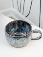 Handmade black, white, and blue glazed ceramic cup, isometric view