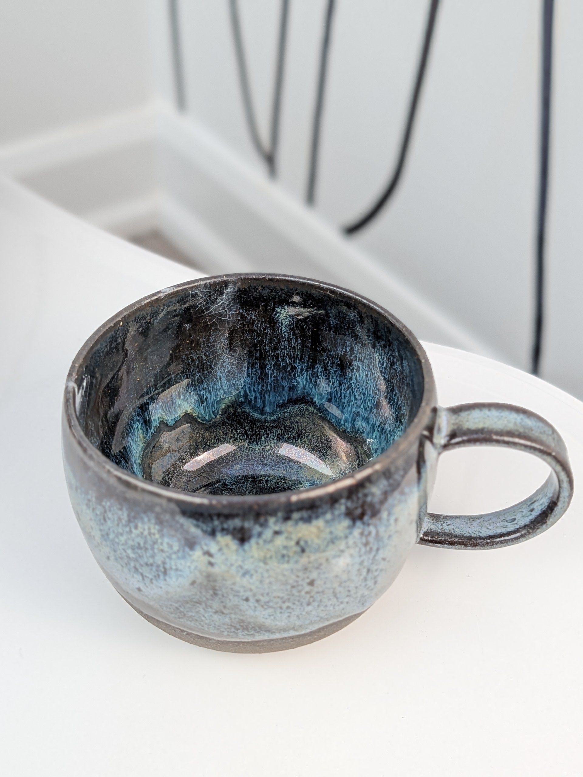 Handmade black, white, and blue glazed ceramic cup, isometric view
