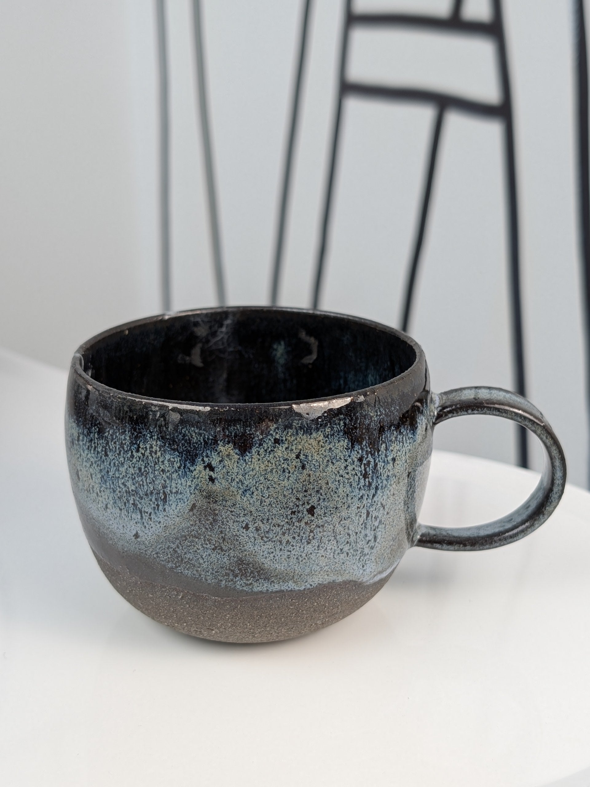 Handmade black, white, and blue glazed ceramic cup, side view with handle