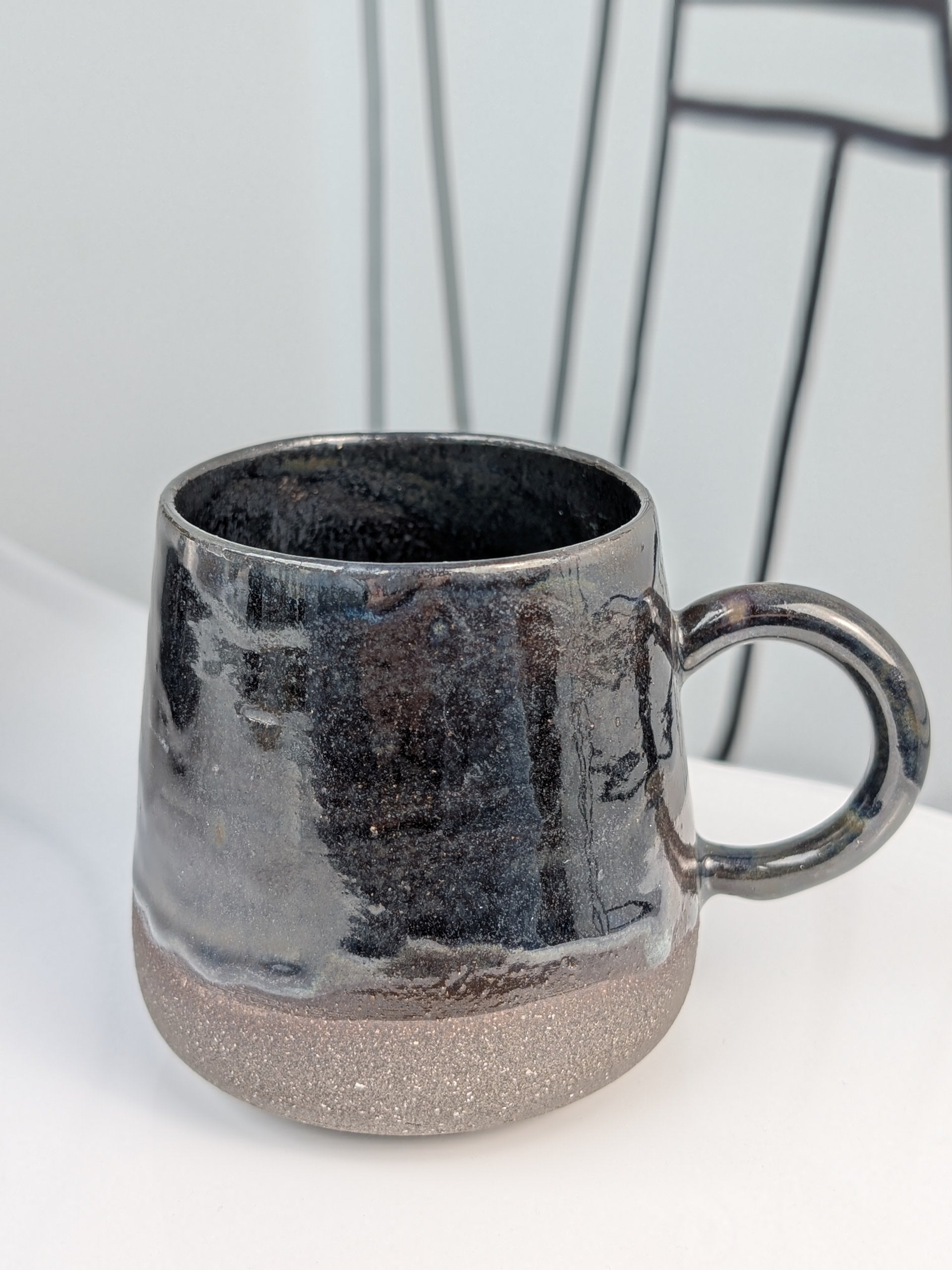 Handmade black glazed ceramic cup, side view with handle