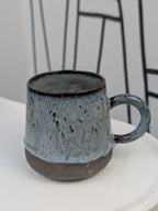 Handmade blue and black glazed ceramic cup, side view with handle