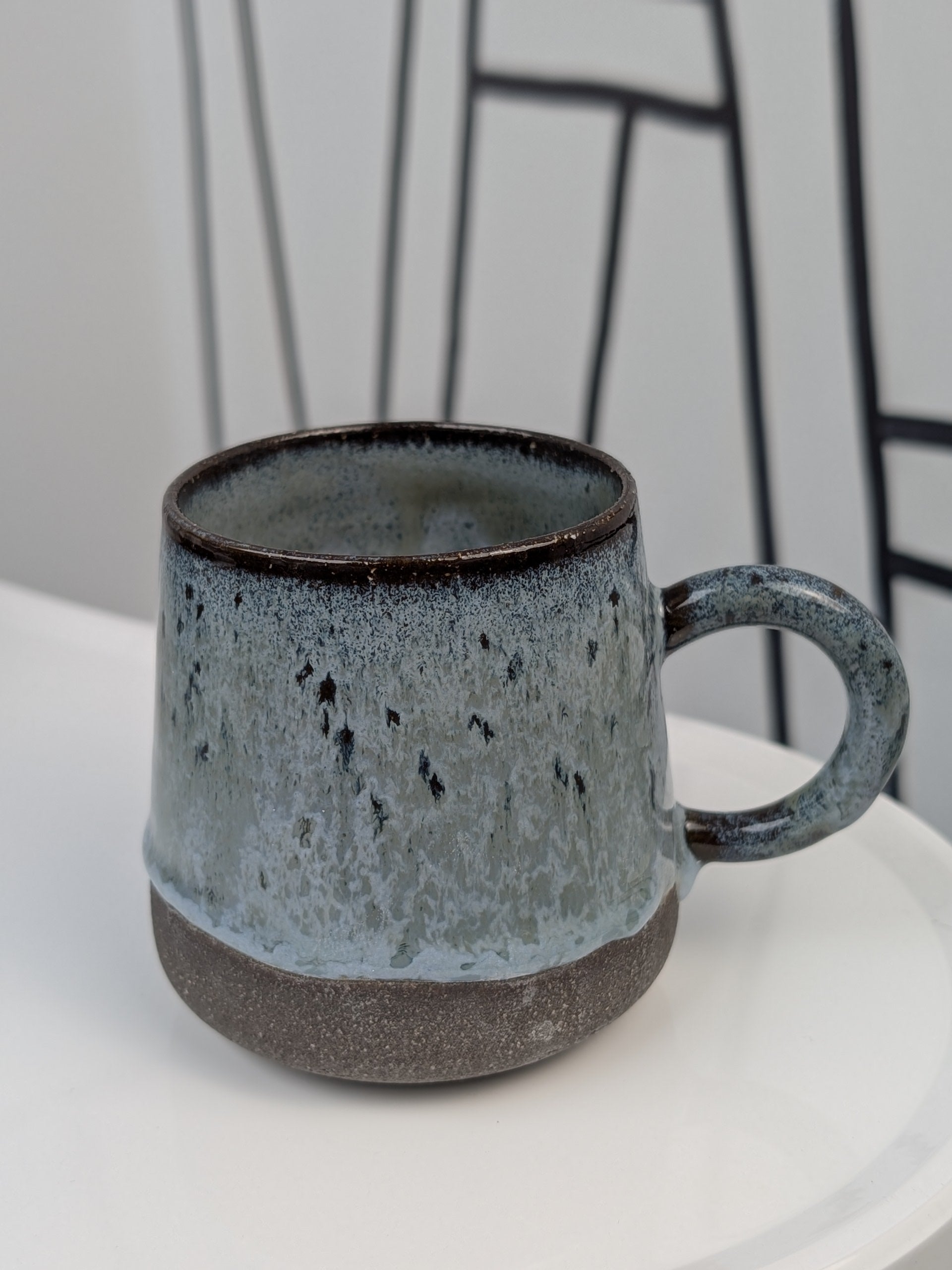 Handmade blue and black glazed ceramic cup, side view with handle