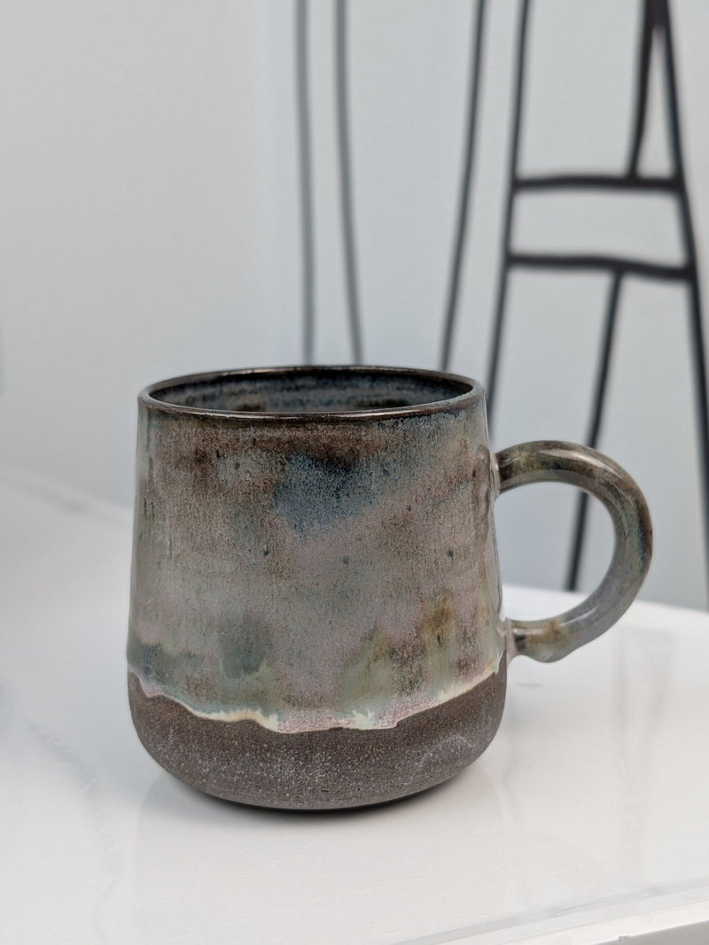 Handmade brown, green, and pink glazed ceramic cup, side view with handle